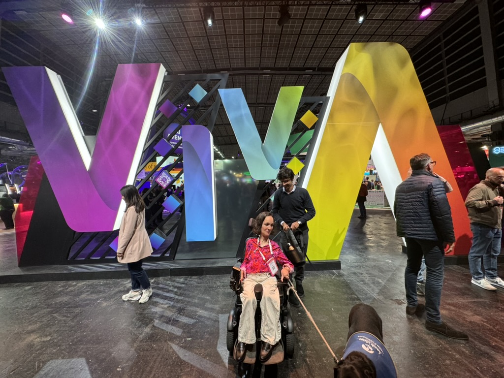 Charlotte dans son fauteuil roulant avec un ami devant le logo du salon VivaTech