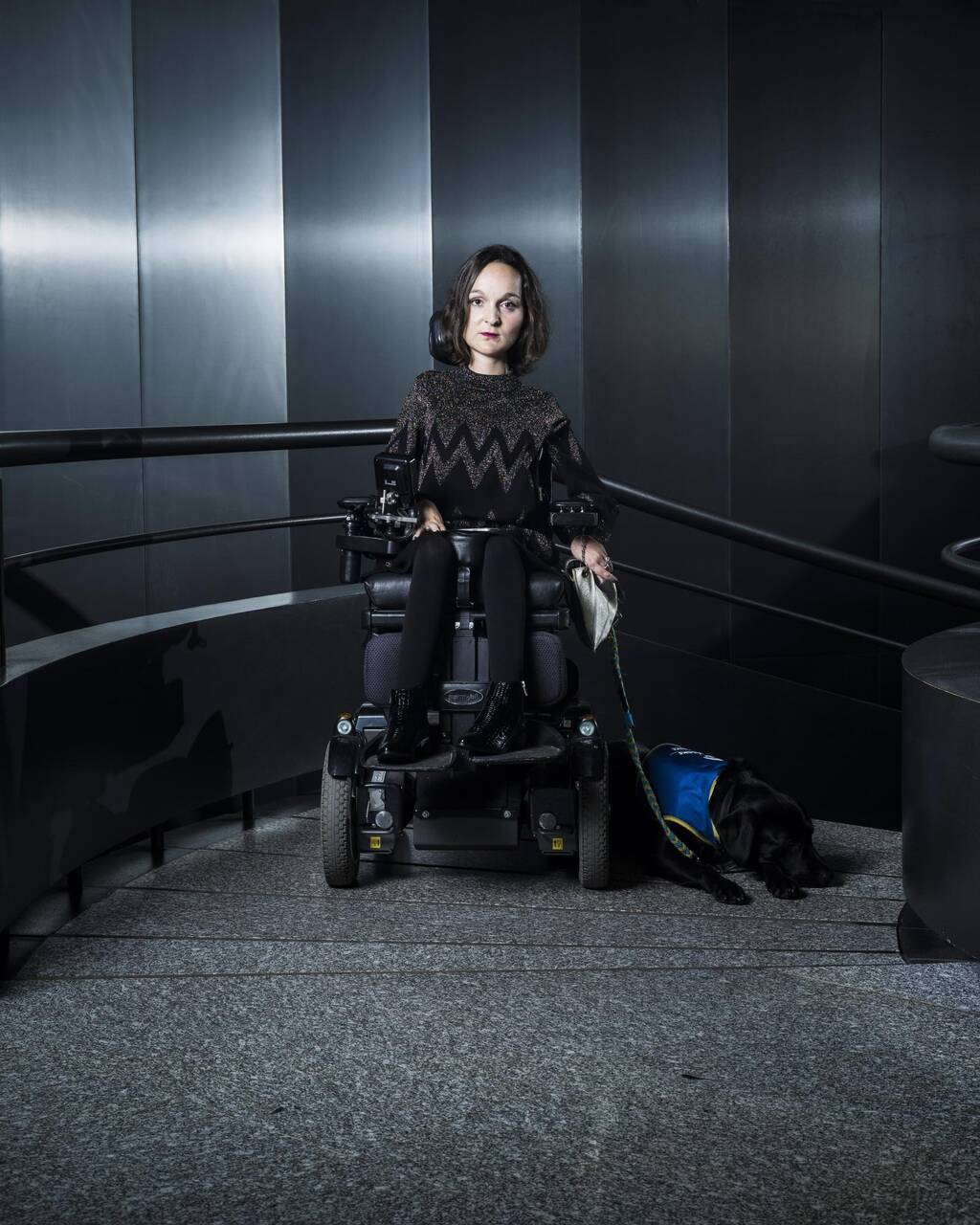 Photo de Charlotte, habillée en noir, dans une cage d'escalier noir. Ambiance Dark Vador.